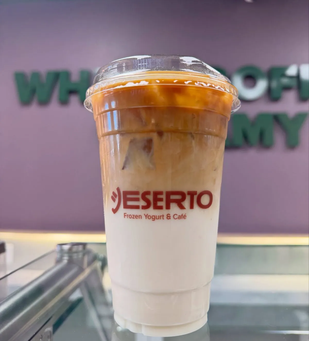 A layered iced coffee in a branded Deserto cup on the café counter