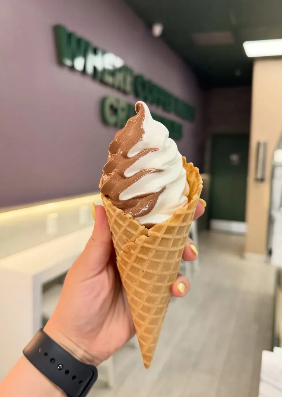 A two-tone chocolate and vanilla swirl in a waffle cone held up in the café's arched hallway